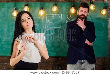 Man With Beard And Young Lady Teacher Stand In Classroom, Chalkboard On Background. Generation Conce