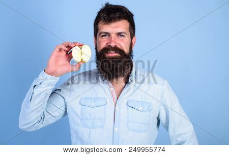 Man Bearded Smiling Holds Apple Blue Background. Half Of Apple Healthy Lifestyle. Nutritional Value 
