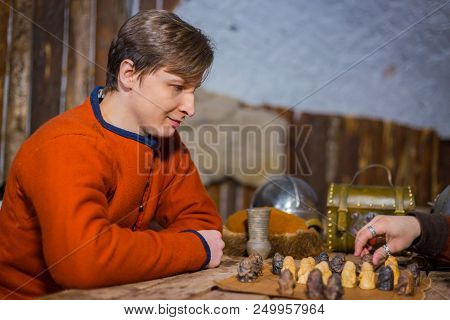Portrait Of Man In Russian Ethnic Suit Playing Board Game Like Chess. Folk, Competition And Traditio