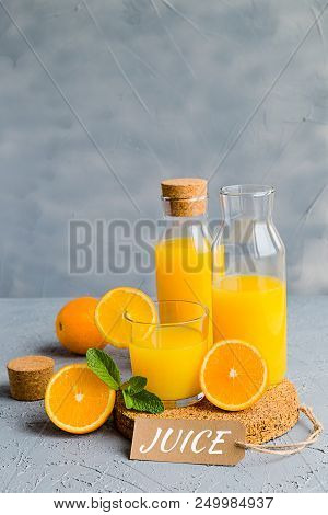 Orange Freshly-squeezed Juice In A Glass And Bottles On Grey Table.