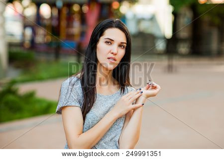 Young Thoughtfull Woman In Gray Shirt With Long Brunette Hair In The Street. Close Up Portrait