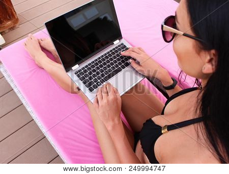 Work And Travel. Incredibly Sexy Girl In A Black Bikini Sits With A Laptop Near The Pool. Find A Tou