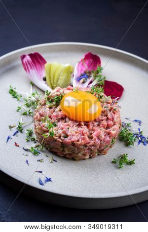 Gourmet tartar raw from beef fillet with yellow of the egg and vegetable as closeup on modern design dish