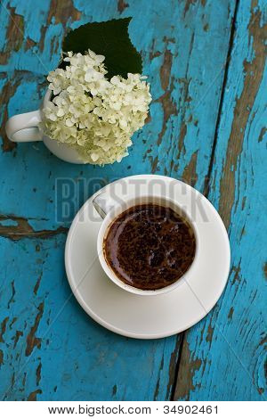 weiÃŸe Tasse mit Kaffee mit Zusammensetzung der weiÃŸen Hortensie auf blauem Hintergrund Holz