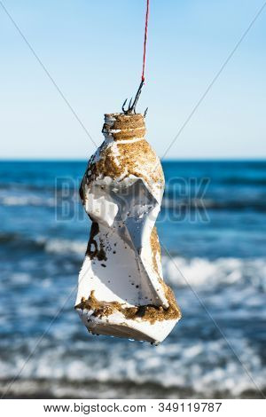 closeup of a used plastic bottle, covered with wet sand, in a fish hook, freshly fished in the ocean, in front of the water