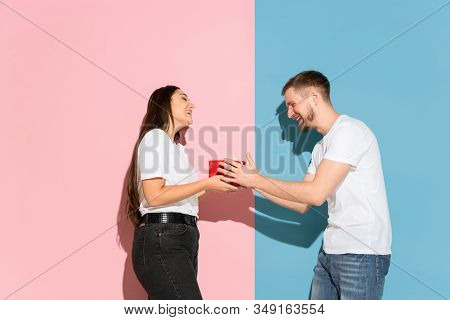 Love. Giving A Gift For St. Valentines Day. Young Man And Woman In Casual Clothes On Pink, Blue Bico