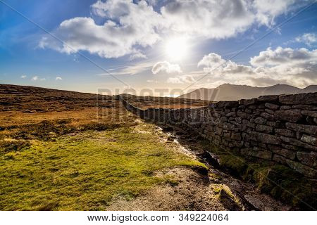 Mourn Wall On The Bank Of Slieve Donard Mountain With Blue Sky, White Clouds And Sunrays. Mourne Mou