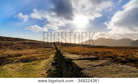 Mourn Wall On The Bank Of Slieve Donard Mountain With Blue Sky, White Clouds And Sunrays. Mourne Mou
