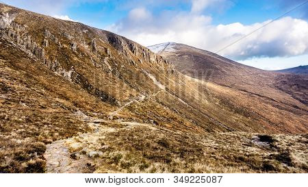 Footpath Leading To Snow Capped Peak Of Slieve Donard Mountain. Mourn Wall Surrounding Mourn Mountai