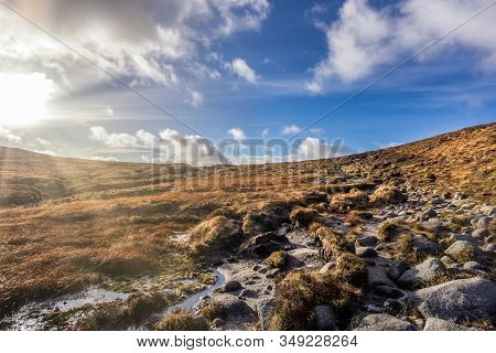 Wet And Rocky Field On The Bank Of Slieve Donard Mountain With Blue Sky, White Clouds And Sunrays. M