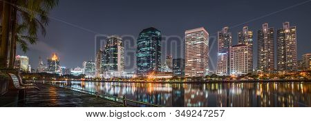 A Bench Near The Lake In Benjakiti Park With Skyscrapers At Night In Bangkok, Thailand