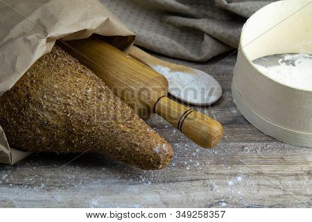 A Loaf Of Bread Along With Rocking For The Dough In A Craft Bag Stand On A Wooden Table, Next To It 
