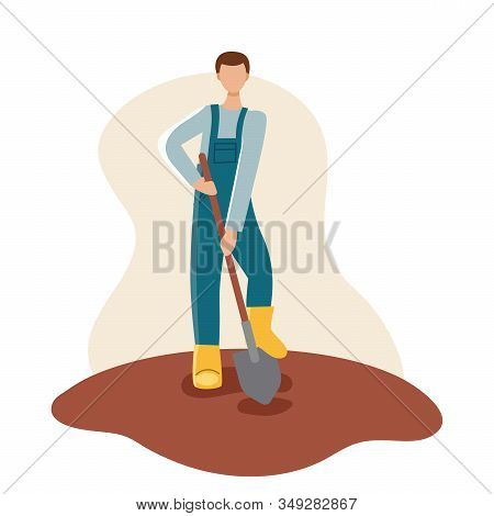 A Male Gardener In A Yellow Boots And Blue Robe Holds A Shovel And Digs Up The Ground. Spring Planti