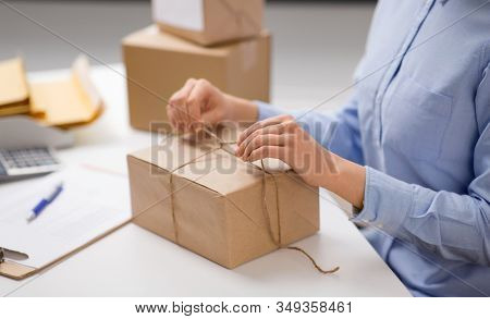 delivery, mail service, people and shipment concept - close up of woman packing parcel box and tying rope at post office