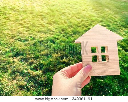 Miniature Wooden House On Green Grass In Female Hands. Real Estate Concept. Modern Housing. Eco-frie