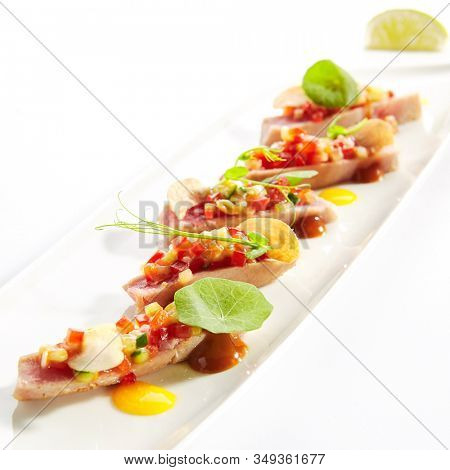 Appetizer with tuna tartar, seasonal vegetables and greens on white restaurant plate isolated. Macro photo of delicious healthy red fish tatar or tar-tar entree closeup