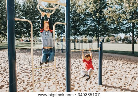 Young Caucasian Boys Friends Hanging On Monkey Bars And Pull-up Bars In Park On Playground. Summer O