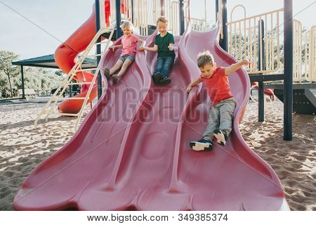 Active Happy Caucasian Children Sliding On Playground Schoolyard Outdoor On Summer Sunny Day. Kid Fr
