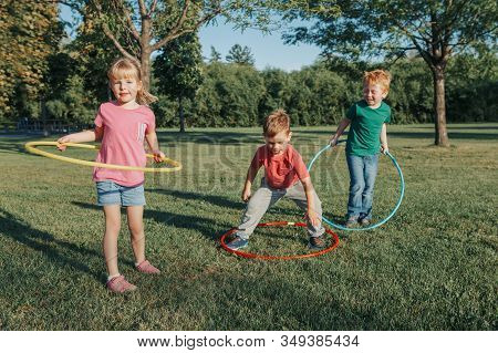 Cute Smiling Caucasian Preschool Girl Boys Friends Playing With Hoola Hoop In Park Outside. Kids Spo