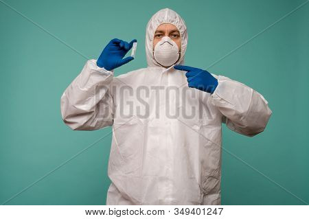 A Male Doctor In Protective Overalls And A Mask Pointing At Ampoule With A Vaccine In His Hands. Cor