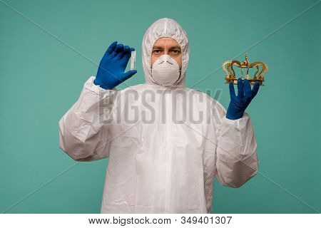 A Male Doctor In Protective Overalls And A Mask Holds An Ampoule With A Vaccine And Crown In His Han
