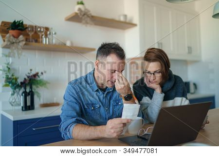 Young Stressed Caucasian Couple Facing Financials Troubles, Sitting At Kitchen Table With Bills, Che
