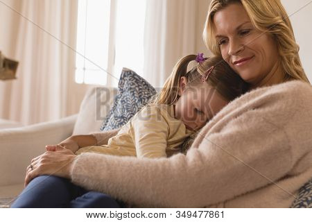 Side view of loving mother embracing her frowning daughter in arms at home