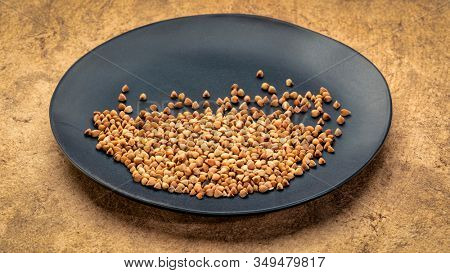 gluten free buckwheat kasha on a black ceramic  plate against textured paper background, healthy eating concept