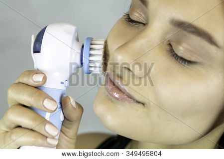 Young Pretty Woman Doing Skin Care Procedure. Cleaning Face With Machine On Grey Background. Copy Sp