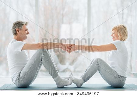 Sports And Healthy Lifestyle.sporty Middle Aged Couple Sitting On The Mat In The White Fitness Gym A