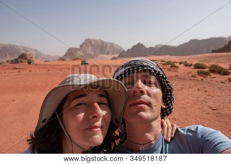 Couple Making A Selfie Photo In Wadi Rum Desert, Jordan. Woman Wearing Hat And The Man A Keffiyeh Pa