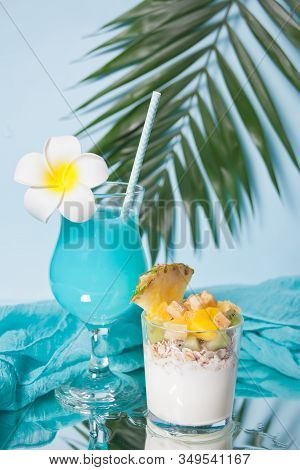 Exotic Tropical Fruit Salad With Muesli And Yogurt In A Glass With Blue Cocktail.