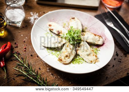 Cooked green mussels with parmegano and cream cheese served on white plate in restaurant