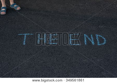 Text The End Underfoot. Feet And Inscription On Asphalt. Notice On Road