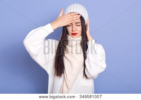 Horizontal Indoor Picture Of Exhausted Ill Sweet Young Lady Closing Eyes, Putting Hand On Forehead, 