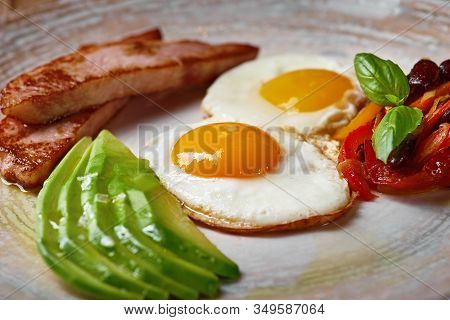 Plate Of Fried Eggs With Bacon And Avocad On Wooden Table. English Breakfast On Table