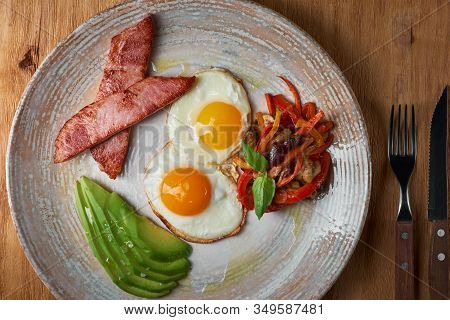 Plate Of Fried Eggs With Bacon And Avocad On Wooden Table. English Breakfast On Table