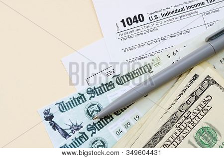 1040 Individual Income Tax Return Form With Refund Check And Hundred Dollar Bills On Beige Backgroun