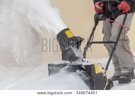 Man Is Brushing White Snow With The Yellow Electric Snow Thrower In A Winter Garden