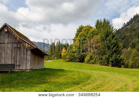 Landscape With Wooden Cottage, Green Meadow, Multi Colored Trees, Mountain Range With Forest And Blu