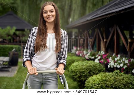 Front View Of Pretty Young Smiling Woman Using Machine On Backyard, Looking At Camera. Portrait Of F