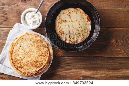 Traditional Russian Crepes Blini Stacked In A Plate And Pancake In A Cast-iron Frying Pan On Dark Wo