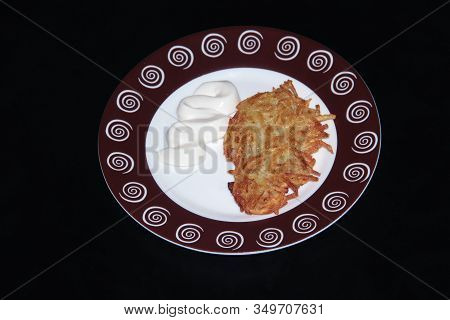 Potato Pancakes With Sour Cream On A Round Plate On A Black Background