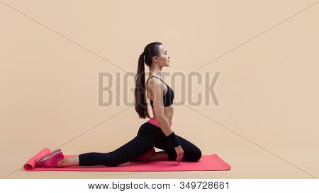 Young Attractive Girl With A Ponytail, Brunette, Sitting In The Pose Of A Pigeon With His Hands On A