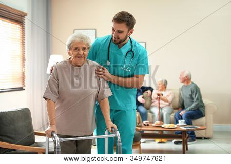 Care Worker Helping To Elderly Woman With Walker In Geriatric Hospice