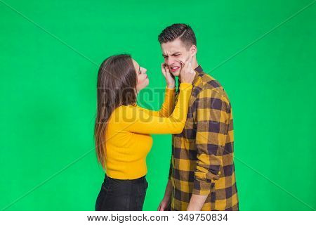 Girl Pinching Guys Cheeks, Making Fyn, He Is Scowling His Face, Looking Completely Annoyed.