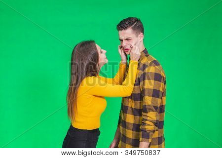 Girl Pinching Guys Cheeks, Making Fyn, He Is Scowling His Face, Looking Completely Annoyed.