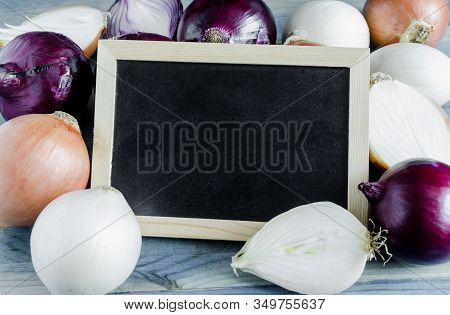 Large Bulbs Of Yellow, White And Red Onions Close-up On A Natural Blue Background Black Board For Te