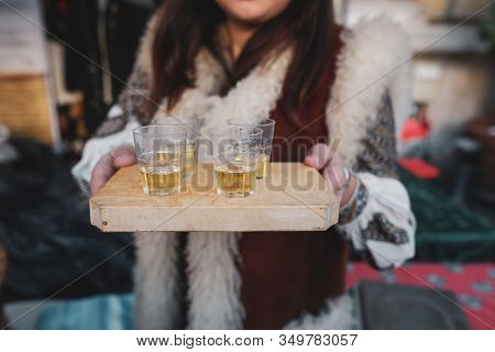 Shallow Depth Of Field (selective Focus) Image With A Woman Holding A Wooden Plate With Palinca (or 