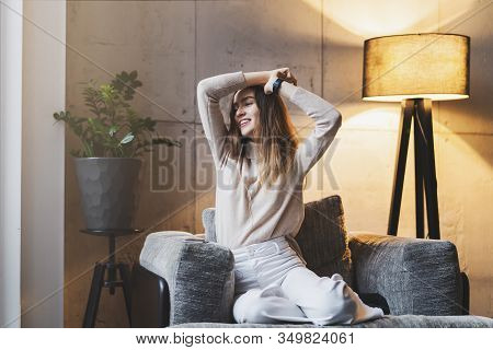 Young Woman Clapping Hands And Laughing. Girl Sitting On Sofa, Listening To Music And Dancing. Relax